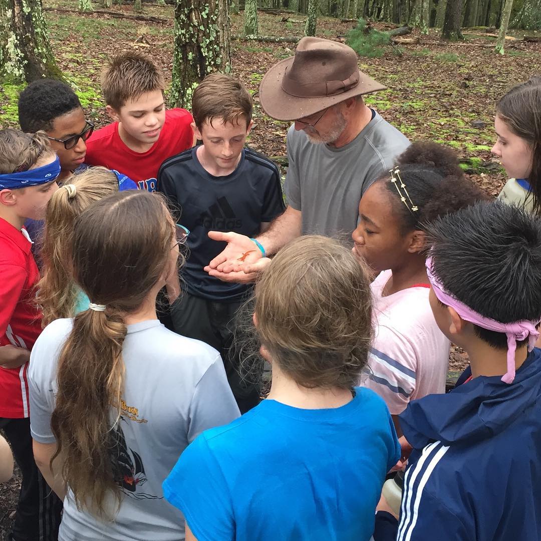 8th grade students inspect an orange salamander with Mr. Danish while on Wilderness